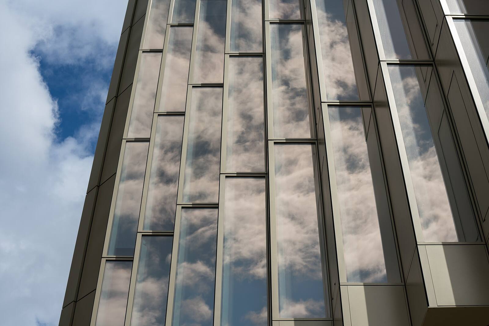 Vertical glass facade panels reflecting clouds and sky